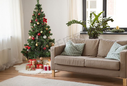 内容引起舒适摄影照片_冬季假期和室内概念—圣诞树，礼物和沙发在舒适的家庭客厅。圣诞树，礼物和沙发在舒适的家里