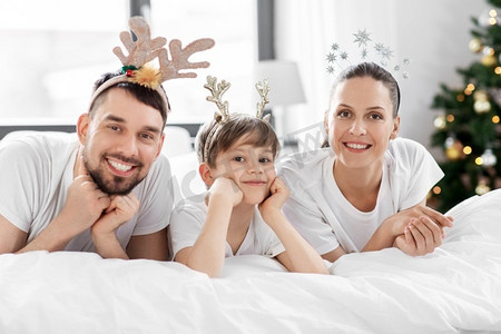 家庭、寒假和人们的概念-圣诞节早晨快乐的父母和小儿子在床上。圣诞节早晨，一家人躺在床上