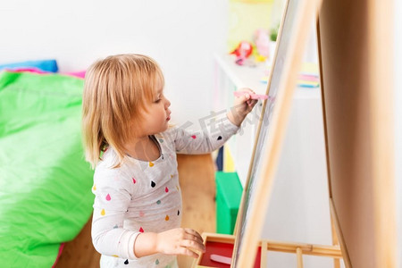 童年，休闲和人的概念—快乐的小女孩画粉笔板在家里。快乐的小女孩画在粉笔板在家里