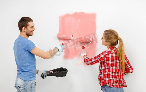 家里墙壁摄影照片_家庭装修概念—快乐夫妇绘画墙壁在家里的时尚颜色2019年活珊瑚。快乐的夫妇画墙在家里