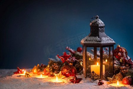 蓝色元宵灯笼摄影照片_燃烧的圣诞灯笼和冷杉装饰在雪在蓝色背景与复制空间。圣诞灯在雪