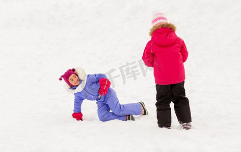 下雪玩耍摄影照片_童年、休闲和季节概念--快乐的小女孩们穿着冬衣在户外的雪地里玩耍。快乐的小女孩在冬天的户外玩耍