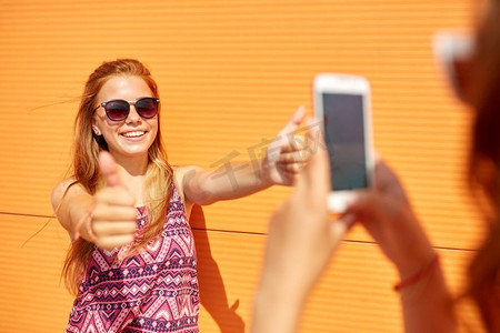 女孩用智能手机拍下她微笑的十几岁朋友夏天在户外竖起大拇指的照片