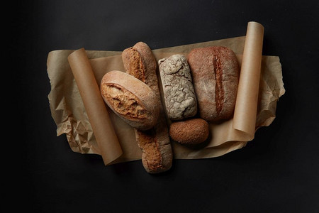 混合新鲜面包在羊皮纸在黑色背景在静物不同类型面包的分类