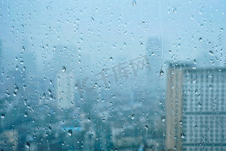 房贷下降摄影照片_雨水滴在窗口玻璃纹理与摩天大楼在背景。雨点落在窗户上