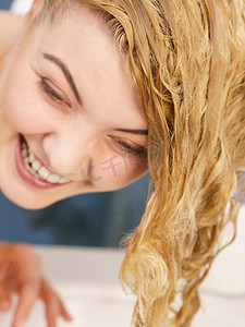 妇女冲洗她的头发，洗出洗发水有潮湿的金发发型在浴室。女人有潮湿的金发