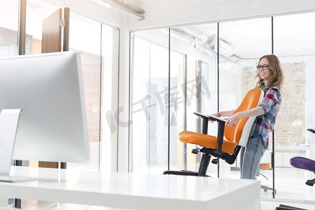 椅子创意摄影照片_微笑的女商人携带橙色椅子在新的办公室