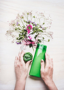 持有绿色化妆品瓶和手工肥皂的女性手在白色背景与植物和花，顶视图天然化妆品概念
