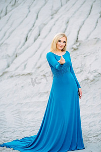 金发女郎在一件蓝色连衣裙与蓝色眼睛在一个花岗岩采石场反对砾石的背景