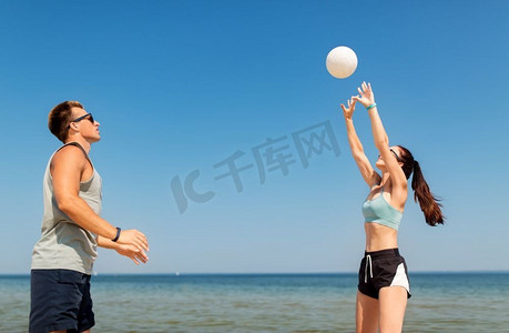 打排球的摄影照片_健身、运动和生活方式理念-夏季海滩上打排球的幸福情侣。夏日沙滩上打排球的幸福夫妻