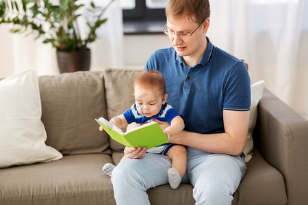 家庭、父亲和人的概念-快乐的父亲和家里有书的小宝贝儿子。快乐的爸爸和小宝贝儿子在家看书