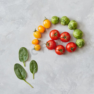 红色和黄色西红柿和绿色菠菜叶组成在灰色背景。俯视图，平面图。番茄和菠菜叶的组成