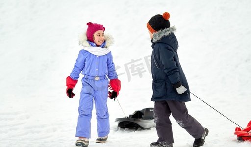 圣诞节小朋友摄影照片_童年、雪橇和季节概念-冬天带着雪橇的快乐小朋友。冬天玩雪橇的快乐小朋友