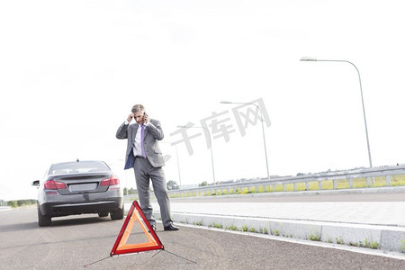 道路故障摄影照片_商人在电话交谈，而站在与故障汽车由道路上的警告标志