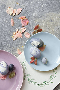蓝色复活节彩蛋与干燥的花瓣和水彩框的石头背景。盘子里的复活节彩蛋