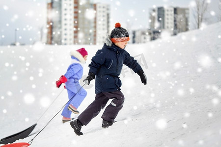 童年，雪橇和季节概念—快乐的小孩子与雪橇爬雪山在冬天。孩子们带着雪橇爬雪山在冬天