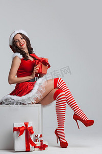 美丽的年轻女孩在圣诞老人的衣服坐在附近的圣诞礼物。带圣诞礼物的女孩