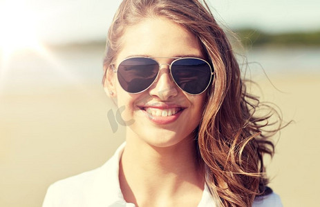 暑假，假日，眼镜和人的概念—微笑的年轻妇女太阳镜在海滩。微笑的年轻女子在太阳镜在海滩
