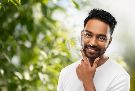 修饰背景摄影照片_修饰和人概念—微笑的印度人触摸他的胡子在绿色自然背景微笑的印度男子触摸他的胡子