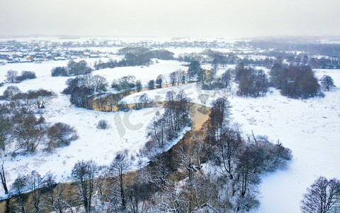 在冬天的雪河鸟瞰图。白俄罗斯明斯克附近的河岸和草地上的冰冻树木。村庄背景
