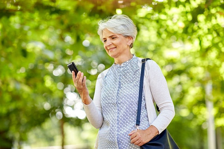 科技、老年和人的概念快乐的老年女性在夏季公园拿着智能手机。夏令营里拿着智能手机的快乐老年女性