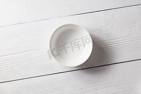 白色陶瓷空盘放在一张白色木桌上，有复印空间。一张白色的木制餐桌上放着一个空盘子。顶视图