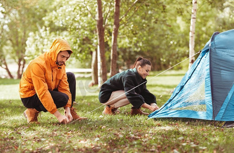 camper摄影照片_露营，旅游和旅行概念—愉快的夫妇设置帐篷户外。快乐的夫妇设置帐篷户外