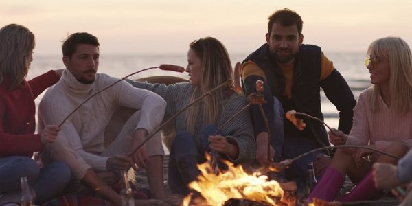 一群年轻的朋友深夜坐在火堆旁，烤香肠，喝啤酒，聊天，玩得很开心