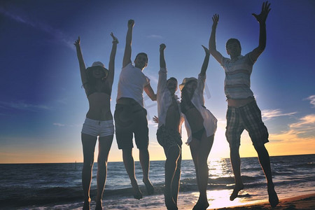 夕阳西下，欢乐青年朋友团在沙滩上跳跃奔跑，尽情玩乐庆祝