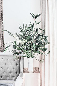现代静物与房子植物在花瓶在沙发，前视图.  竹束排列与热带树叶和树枝在白色墙壁在家里