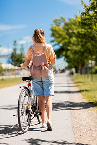 人，休闲和生活方式—年轻妇女与自行车和背包走在城市街道。妇女与自行车和背包走在城市