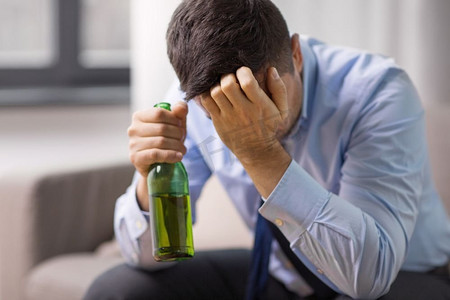 男性下体痛摄影照片_酒精中毒、酒精成瘾和人们的观念——男性酗酒者在家喝瓶装啤酒。男性酗酒者在家喝啤酒