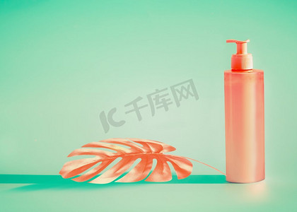 防晒护肤品摄影照片_粉红色化妆瓶，带有分配器泵和薄荷背景下的热带叶子。夏季护肤品或防晒品，有设计的文案空间