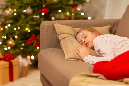 漂亮女孩理头发摄影照片_圣诞节、假日和童年概念—女孩睡在家里的沙发上。女孩睡在沙发上在圣诞节