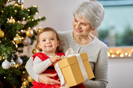 圣诞节，假日和家庭概念—快乐的祖母和婴儿孙女与礼物在家里。祖母和女婴与圣诞礼物