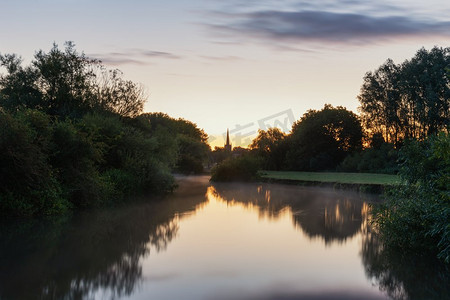 英国科茨沃尔德乡村泰晤士河畔莱克莱德美丽的日出景观，背景是教堂尖顶