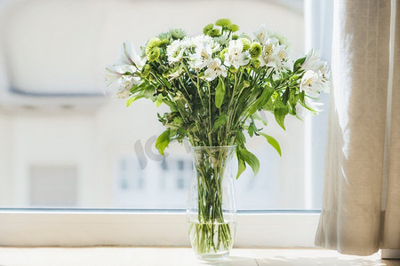 美丽的绿色花朵束在花瓶在窗口。家居室内装饰