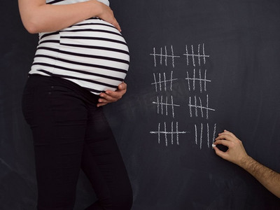 怀孕的夫妇记录怀孕的一周。一对年轻的怀孕夫妇用粉笔在黑板上写下怀孕周的情况