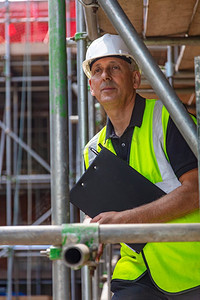 男建筑工头、建筑工人或工地经理，手持剪贴板，头戴白色安全帽，身穿高空背心