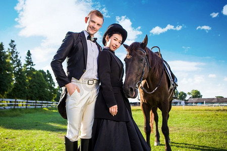 肖像自信的穿着得体的夫妇站在与马的领域