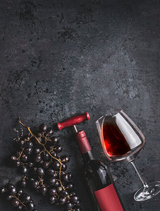 红葡萄酒瓶与葡萄酒开塞螺丝，玻璃和葡萄在复古黑色背景，顶视图.