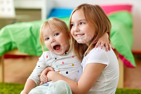 童年、家庭、表情和人概念-拥抱在家的愉快的小女孩或姐妹。快乐的小女孩或姐妹在家里拥抱