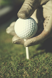 高尔夫球员把球放在球座上。在高尔夫球场风景的美丽的日出在背景中。高尔夫球员将球放置在球座上