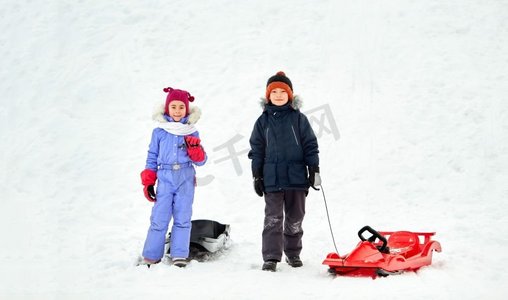 圣诞节小朋友摄影照片_童年、雪橇和季节概念-冬天带着雪橇的快乐小朋友。冬天玩雪橇的快乐小朋友