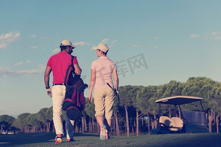 年轻夫妇走到下一个洞在高尔夫球场上。一个拿着高尔夫球袋的男人。夫妇走在高尔夫球场