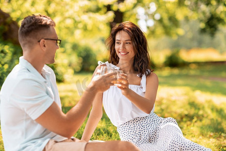 休闲与人概念—快乐夫妇在夏季公园野餐饮料。快乐的夫妇干杯饮料在夏季公园