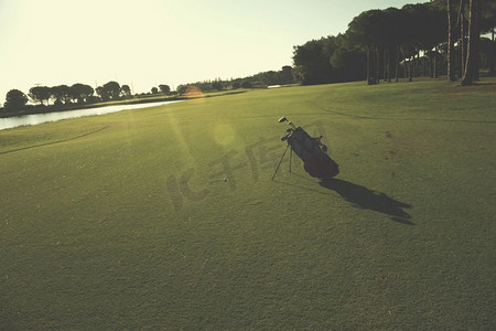 球场上的高尔夫球袋，在美丽的日出时，球杆和球在前面。高尔夫球场上的高尔夫球包