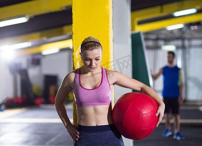 美丽的运动员妇女的肖像与红色的医疗球在crossfit健身房。肖像的女人与红色交叉健身球