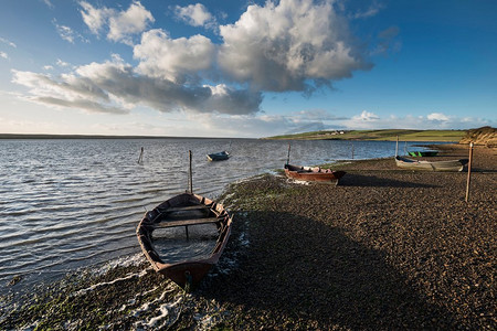 美丽、朝气蓬勃的日落风光映衬着停泊在海边的小船。停泊在英国多塞特郡舰队泻湖的美丽日落风景画