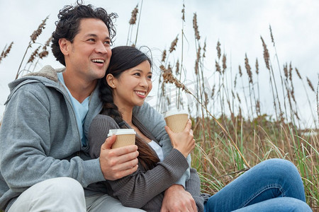 年轻的亚洲人中国男人和女人，男孩女孩，有完美牙齿的夫妇坐在海滩喝外卖杯茶或咖啡